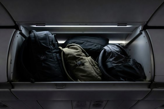 Interior overhead compartment of an airliner with fitted backpacks under high contrast cabin lighting