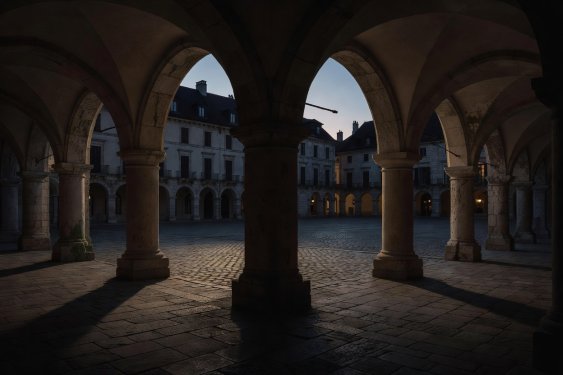 Historic stone arcade with deep evening shadows overlooking a quiet pedestrian plaza